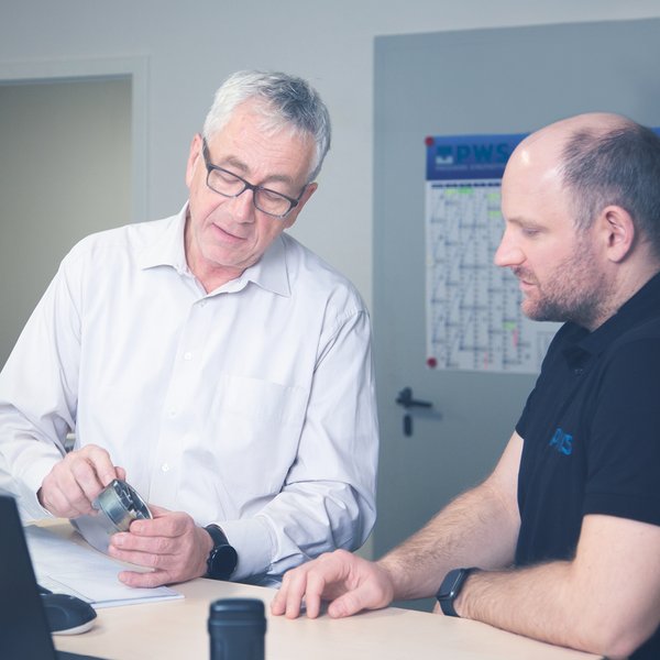 Two men are looking at a piece of metal that one of them is holding.