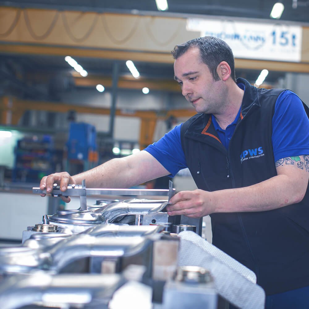 mann arbeitet an einem Fließband, auf dem sich mehrere Metallwerkstücke befinden.