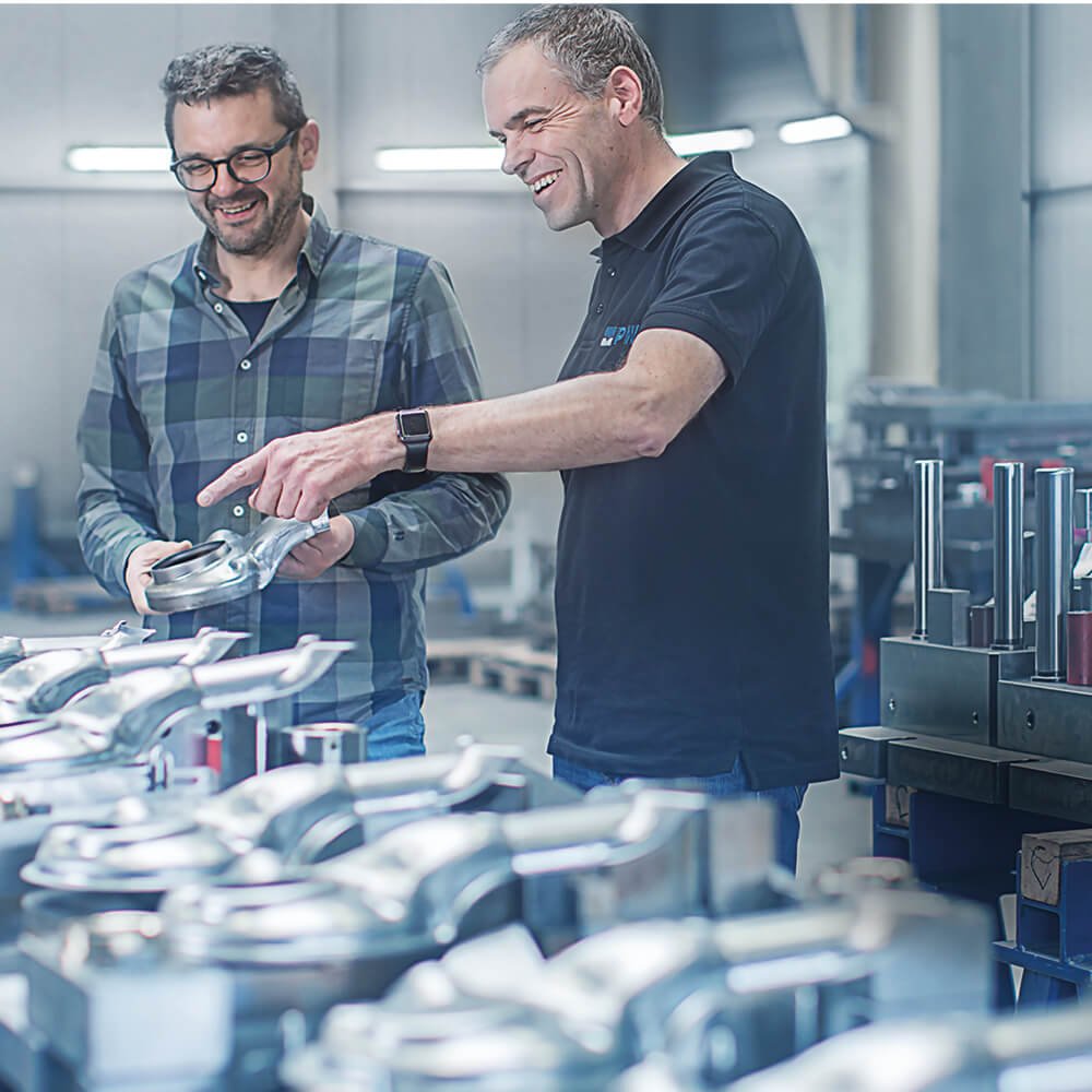 Zwei Männer die auf eine Reihe von Werkstücken aus Metall sehen.