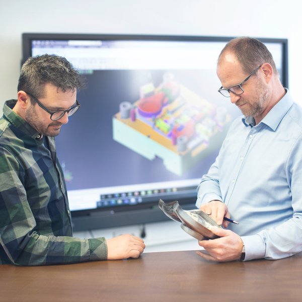 Two men are looking at a piece of metal that one of them is holding.